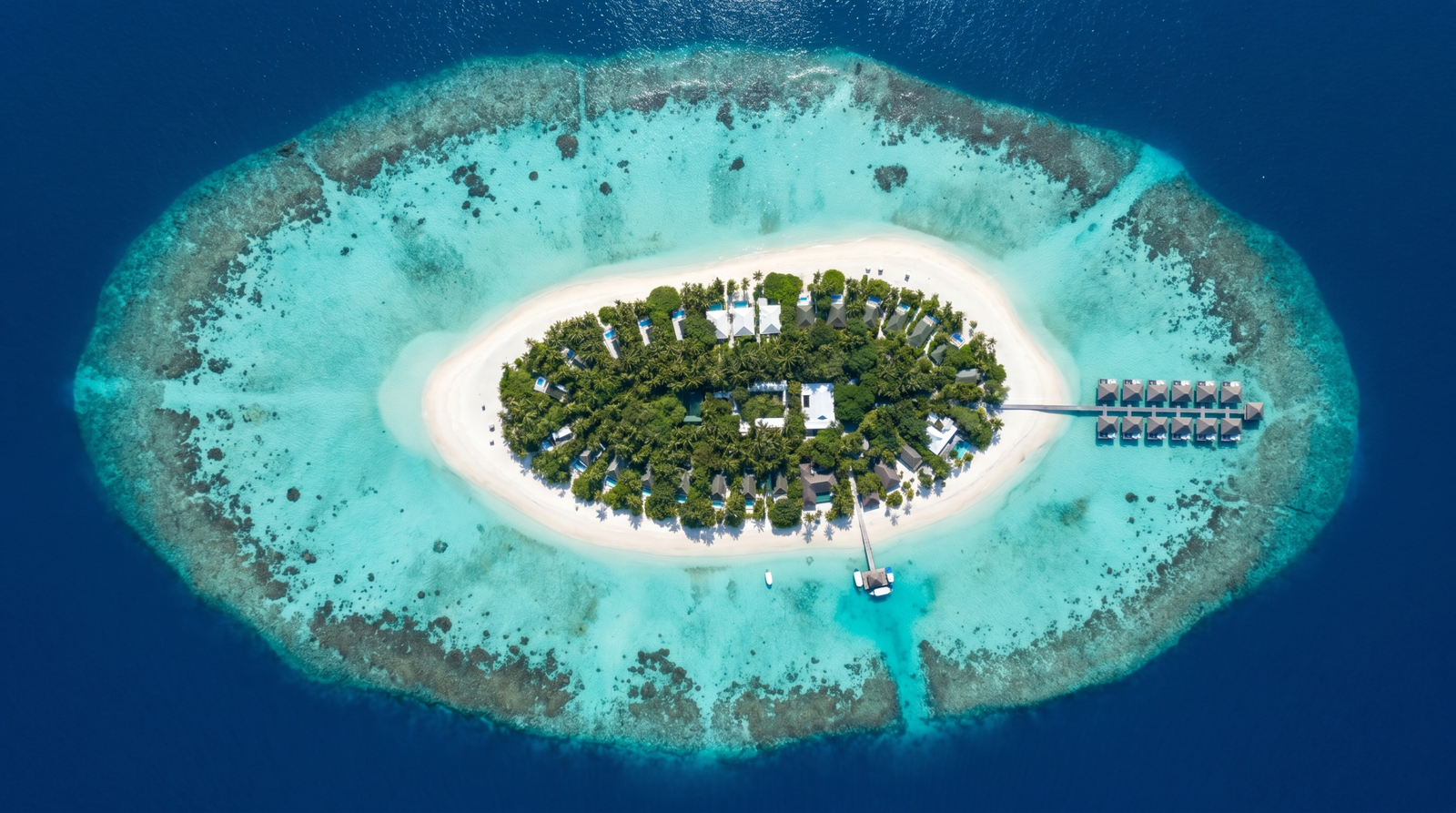 Aerial drone view of Maldives resort island — circular island surrounded by turquoise lagoon and coral reef, Indian Ocean